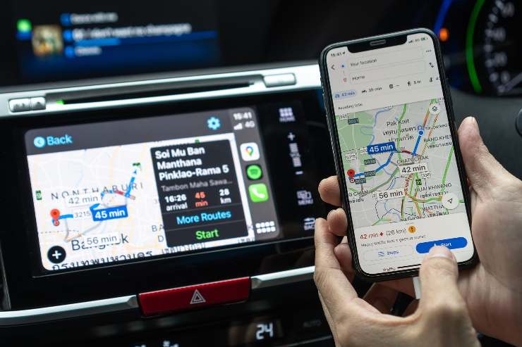 Infotaiment di un'auto e una persona che tiene in mano uno smartphone con google maps aperto