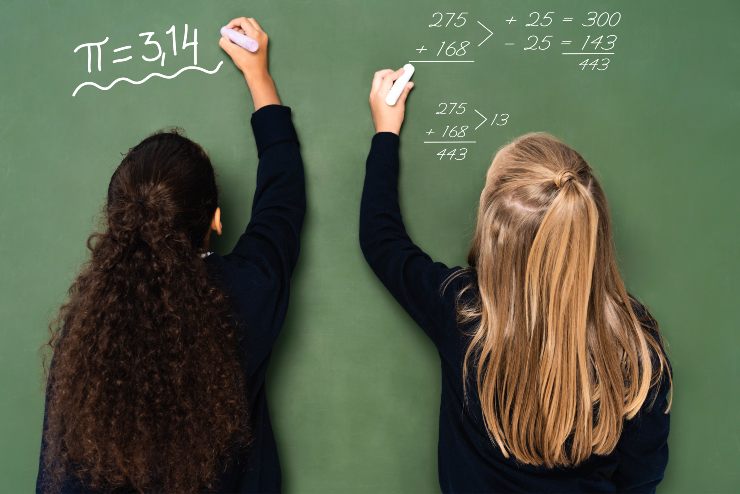 Due ragazze alla lavagna che scrivono formule matematiche (Depositphotos)