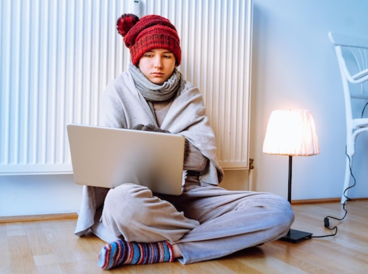 Donna infreddolita accanto al termosifone e al pc