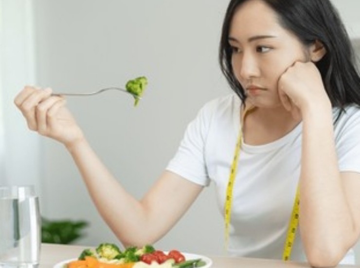 Giovane donna asiatica con piatto di verdure davanti