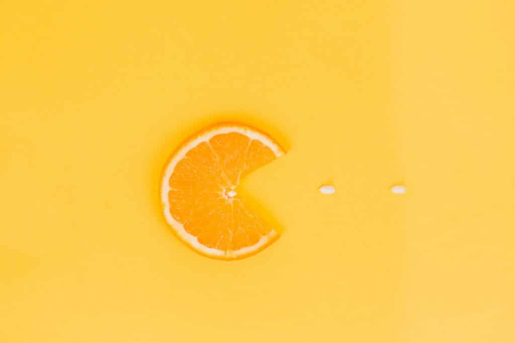 Foto artistica con agrumi: fetta d'arancio e due semi su sfondo giallo richiamano Pac-Man