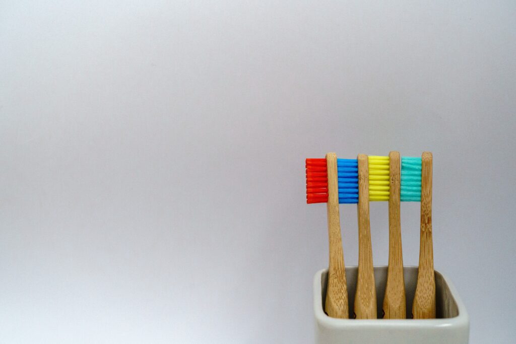 Tre spazzolini in bamboo in porta spazzolino su sfondo bianco e con setole colorate in rosso, blu, giallo, verde acqua.