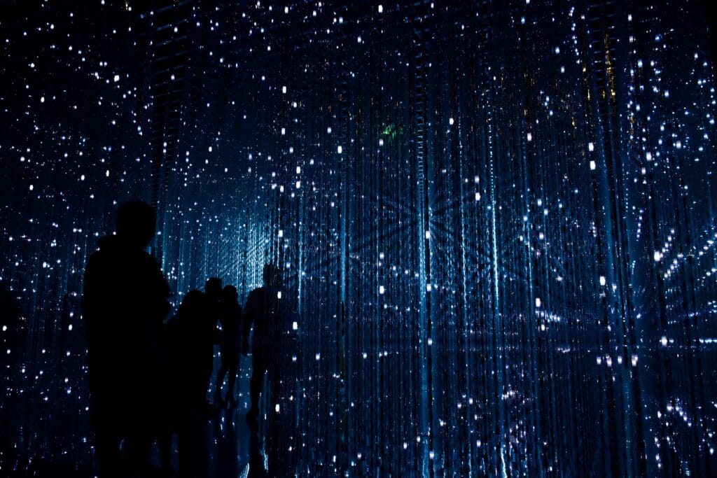 immagine astratta con figure umane in nero su sfondo blu stellato e striato da scie luminose