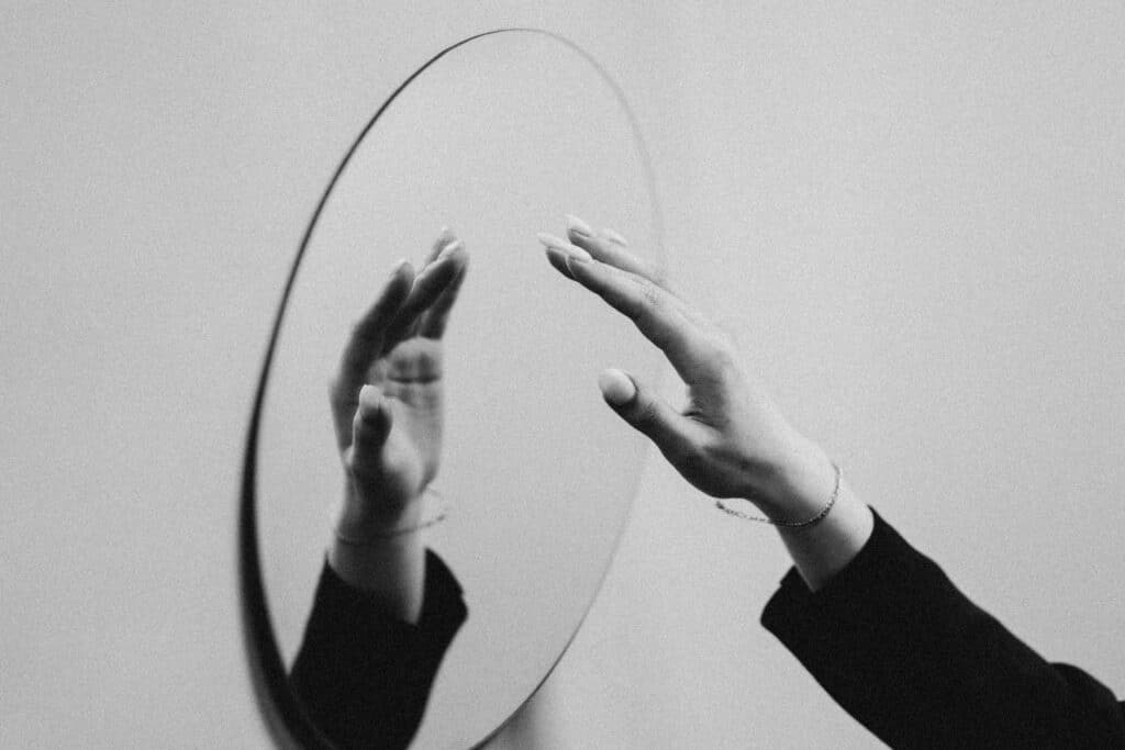 foto in bianco e nero di una mano che ta per toccare uno specchio e che si riflette in esso