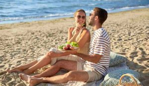 Coppia sulla spiaggia che mangia frutta e verdura