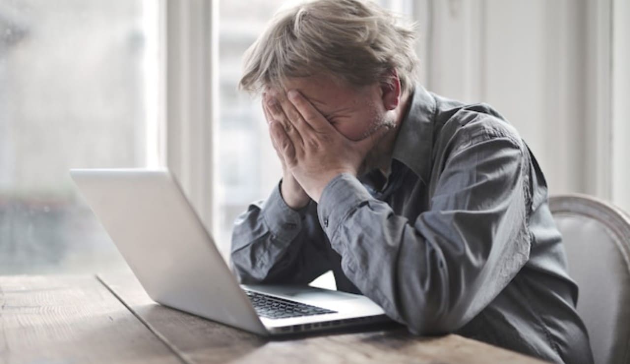 Uomo disperato al suo PC con le mani in volto