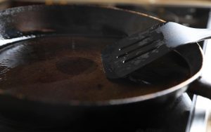 Padella con spatola e olio da cucina usato sul fornello, primo piano